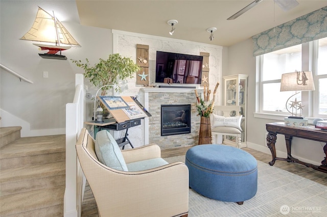 sitting room with stairway, a ceiling fan, a stone fireplace, wood finished floors, and baseboards