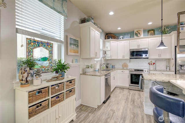 kitchen with stainless steel appliances, white cabinetry, a sink, and light stone counters