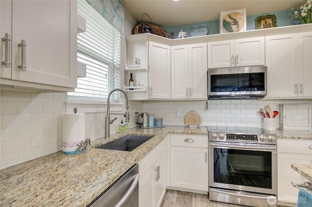 kitchen with light stone counters, tasteful backsplash, appliances with stainless steel finishes, white cabinets, and a sink