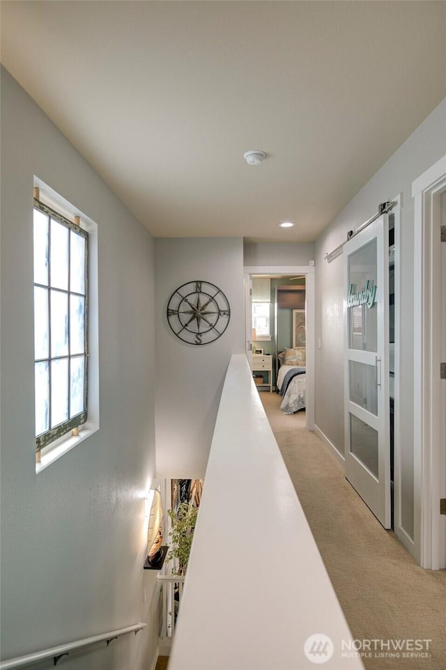 hall featuring a barn door, an upstairs landing, and light colored carpet