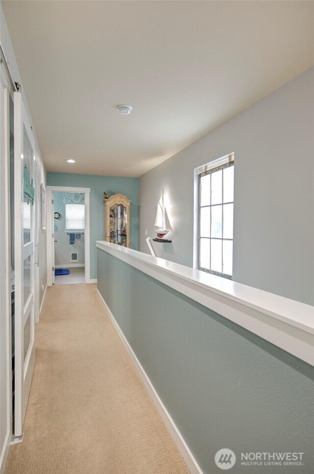 corridor with baseboards and light colored carpet