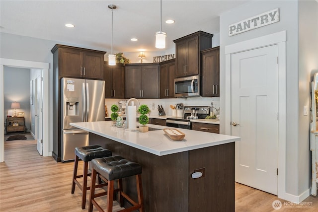 kitchen with dark brown cabinetry, stainless steel appliances, a sink, and light wood finished floors