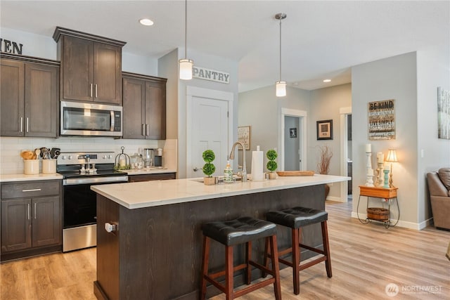 kitchen with light wood-type flooring, dark brown cabinetry, appliances with stainless steel finishes, and decorative backsplash