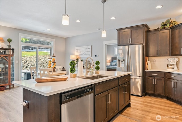 kitchen featuring a sink, light countertops, appliances with stainless steel finishes, light wood-type flooring, and tasteful backsplash