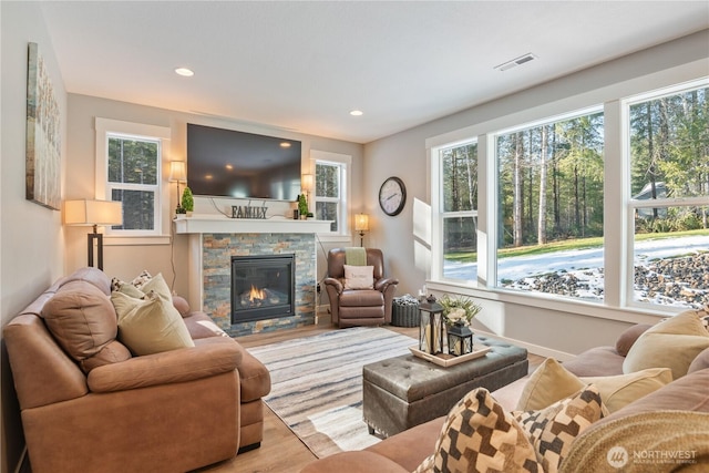 living room with plenty of natural light, visible vents, wood finished floors, and a stone fireplace