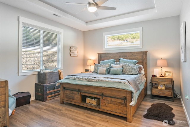 bedroom featuring a tray ceiling, visible vents, baseboards, and wood finished floors