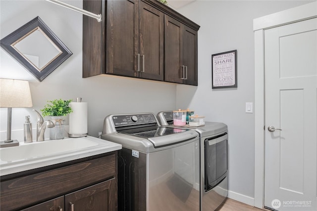 laundry room featuring washing machine and dryer, cabinet space, a sink, and baseboards