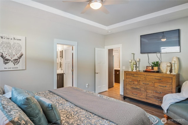 bedroom with ceiling fan, a tray ceiling, connected bathroom, and wood finished floors