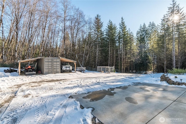 snowy yard featuring a detached garage and a view of trees