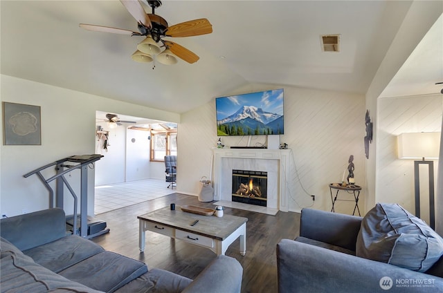 living area with visible vents, vaulted ceiling, wood finished floors, and a tile fireplace