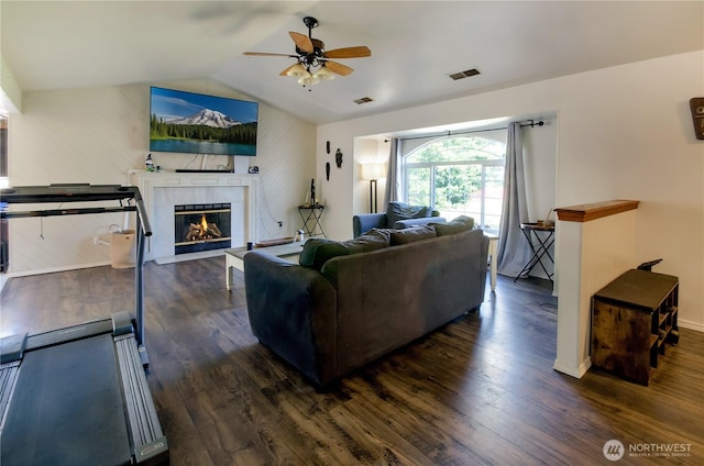 living area with dark wood-type flooring, visible vents, a ceiling fan, vaulted ceiling, and a tiled fireplace