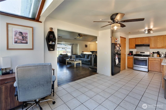 kitchen with freestanding refrigerator, under cabinet range hood, stainless steel gas range oven, and light tile patterned floors