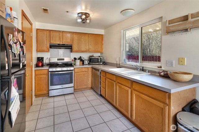 kitchen with light countertops, appliances with stainless steel finishes, light tile patterned flooring, a sink, and under cabinet range hood