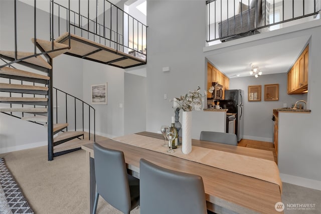 dining area featuring stairway, light colored carpet, a towering ceiling, and baseboards