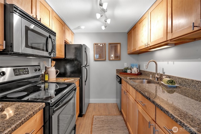 kitchen featuring appliances with stainless steel finishes, a sink, dark stone countertops, light wood-type flooring, and baseboards