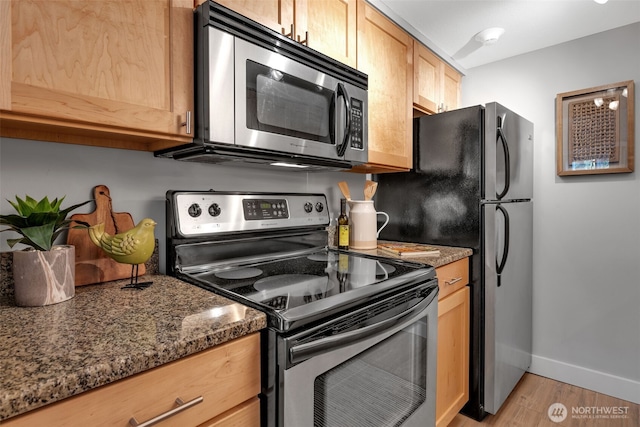 kitchen featuring baseboards, dark stone counters, appliances with stainless steel finishes, light wood-type flooring, and light brown cabinets