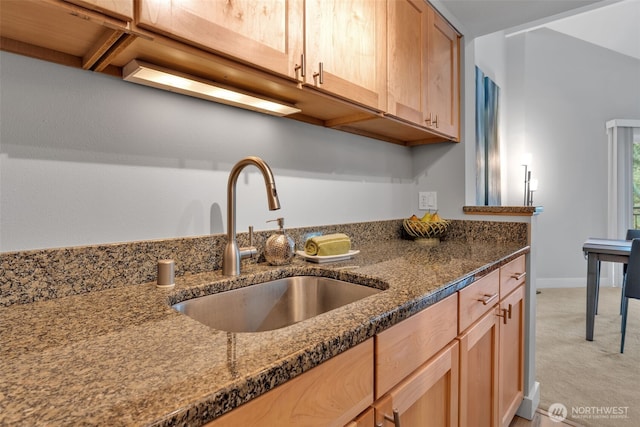 kitchen featuring dark stone counters, light colored carpet, a sink, and light brown cabinets