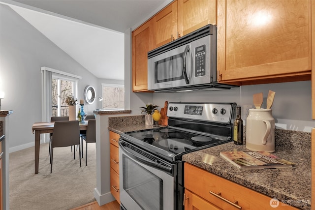 kitchen with stainless steel appliances, light carpet, vaulted ceiling, dark stone countertops, and baseboards