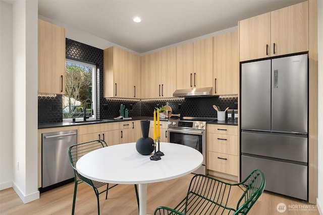 kitchen with light brown cabinets, under cabinet range hood, stainless steel appliances, a sink, and dark countertops