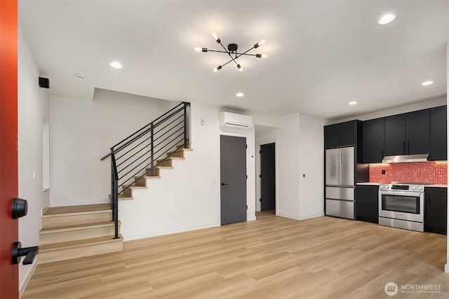 kitchen with dark cabinetry, decorative backsplash, appliances with stainless steel finishes, light wood-type flooring, and a wall mounted air conditioner