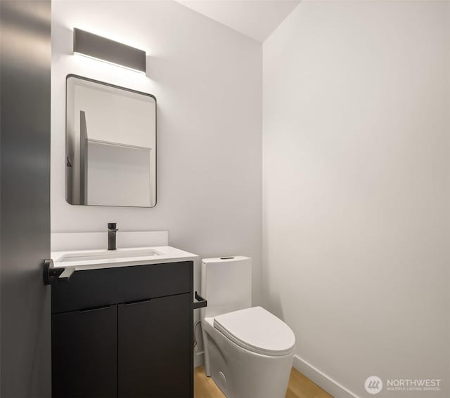 half bath with toilet, baseboards, and vanity