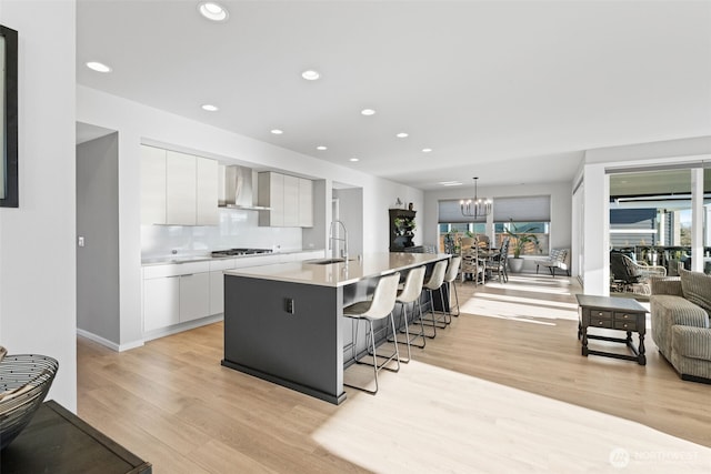 kitchen with white cabinets, wall chimney exhaust hood, modern cabinets, a chandelier, and a sink