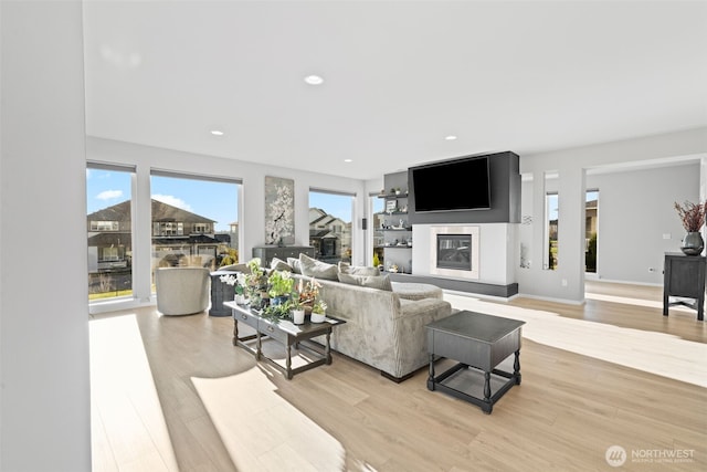 living room featuring baseboards, light wood-type flooring, a glass covered fireplace, and recessed lighting