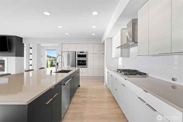 kitchen with wall chimney range hood, modern cabinets, appliances with stainless steel finishes, and a sink