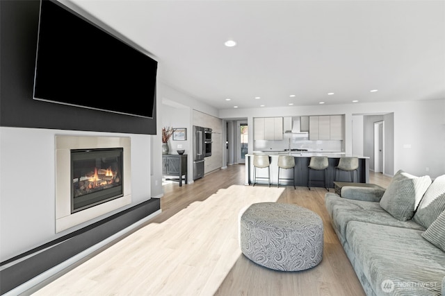 living room featuring light wood-type flooring, a glass covered fireplace, and recessed lighting