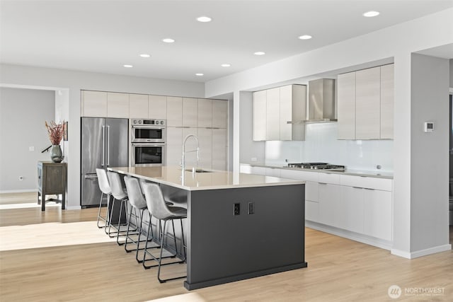 kitchen featuring wall chimney exhaust hood, modern cabinets, appliances with stainless steel finishes, and a sink