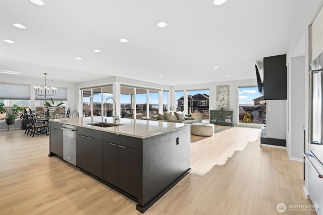 kitchen featuring a chandelier, a sink, light wood-style floors, light countertops, and a center island with sink