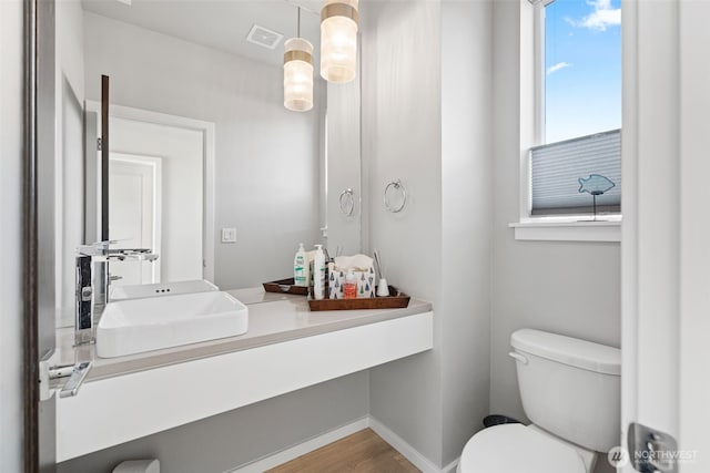 half bathroom featuring toilet, wood finished floors, visible vents, vanity, and baseboards