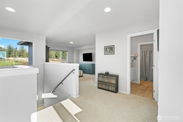 corridor featuring light carpet, recessed lighting, baseboards, and an upstairs landing