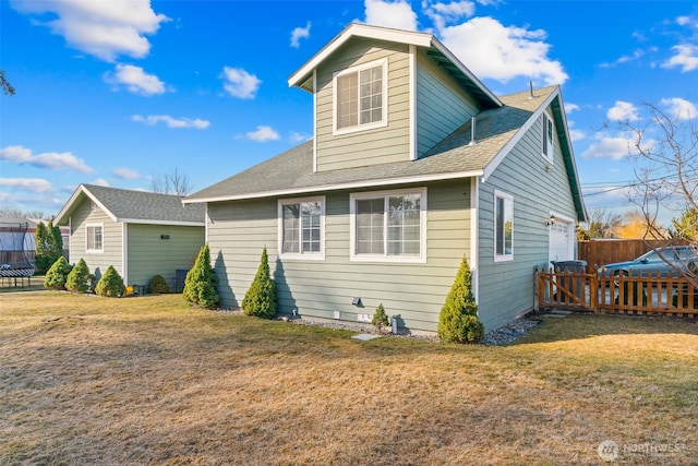 back of house with a shingled roof, a yard, and fence