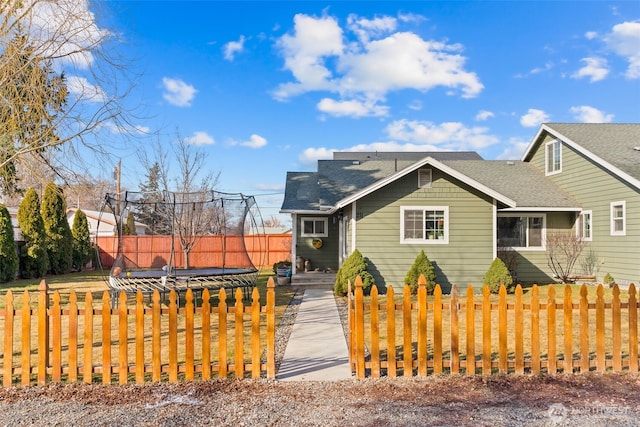 view of front of property featuring a shingled roof, a trampoline, and a fenced front yard