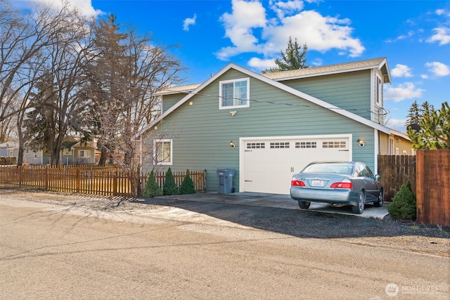 view of side of home with a garage, a fenced front yard, and dirt driveway