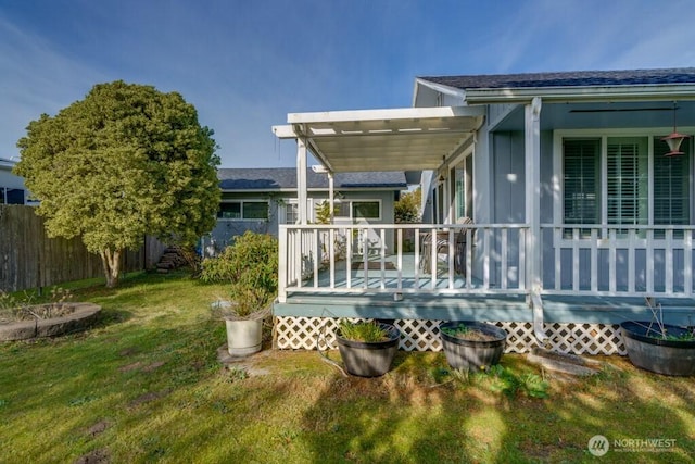 rear view of house featuring fence, a deck, and a lawn