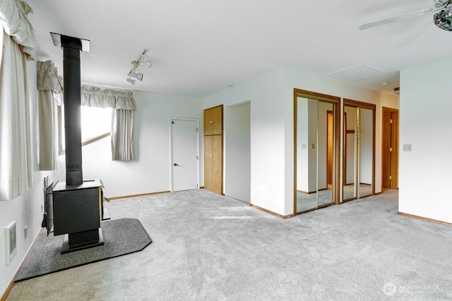 carpeted empty room with a wood stove, ceiling fan, and baseboards