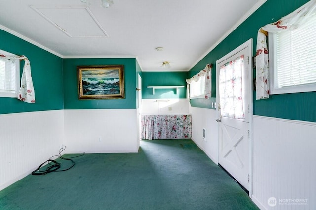 carpeted empty room with a wainscoted wall, attic access, and ornamental molding