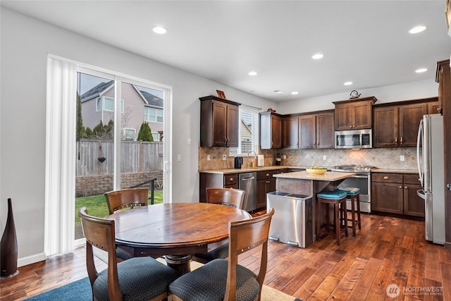 kitchen with a kitchen island, appliances with stainless steel finishes, dark wood-style flooring, dark brown cabinets, and backsplash