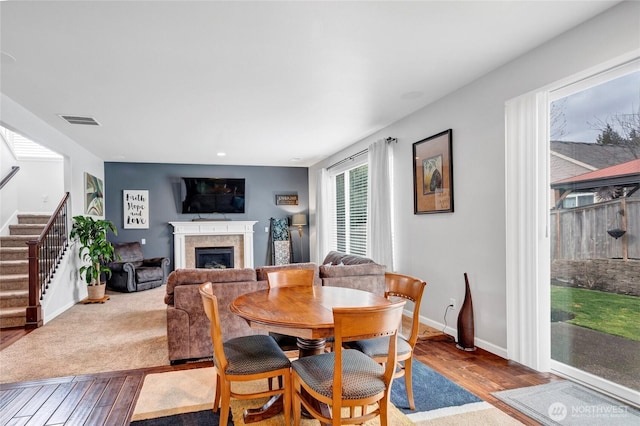 dining space with a fireplace, wood finished floors, visible vents, baseboards, and stairs