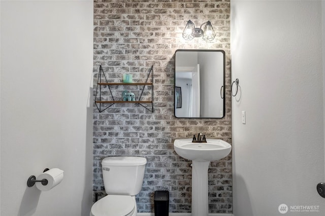 bathroom featuring toilet, brick wall, and a sink