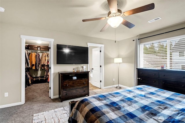 bedroom with baseboards, visible vents, light colored carpet, ceiling fan, and a walk in closet