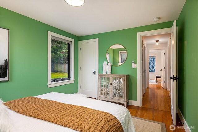 bedroom with multiple windows, baseboards, and wood finished floors