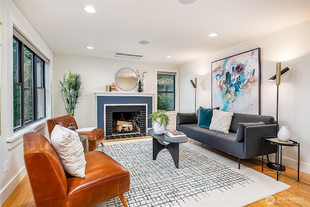 living room featuring wood finished floors, visible vents, baseboards, a fireplace with flush hearth, and recessed lighting