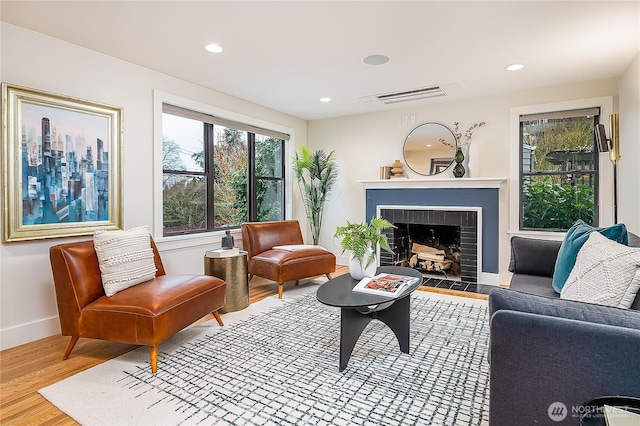 living room with wood finished floors, visible vents, baseboards, recessed lighting, and a brick fireplace