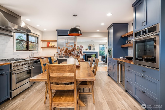 kitchen featuring light wood-type flooring, high quality appliances, open shelves, a sink, and wall chimney exhaust hood