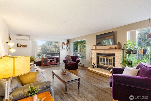 living area featuring a fireplace, a baseboard heating unit, an AC wall unit, a textured ceiling, and wood finished floors