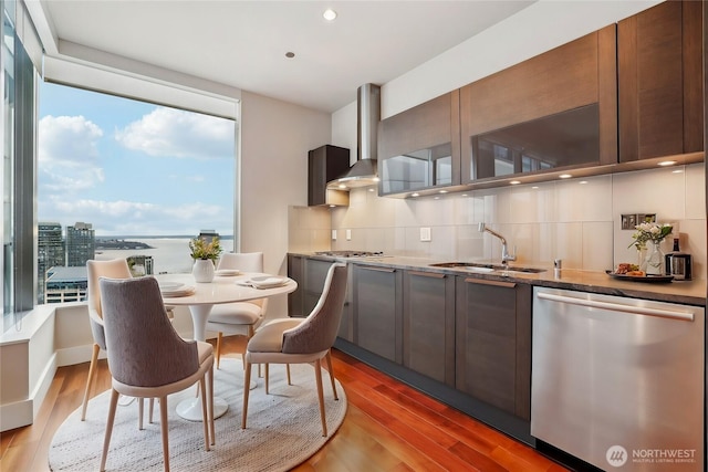 kitchen with a sink, appliances with stainless steel finishes, wall chimney range hood, backsplash, and light wood finished floors