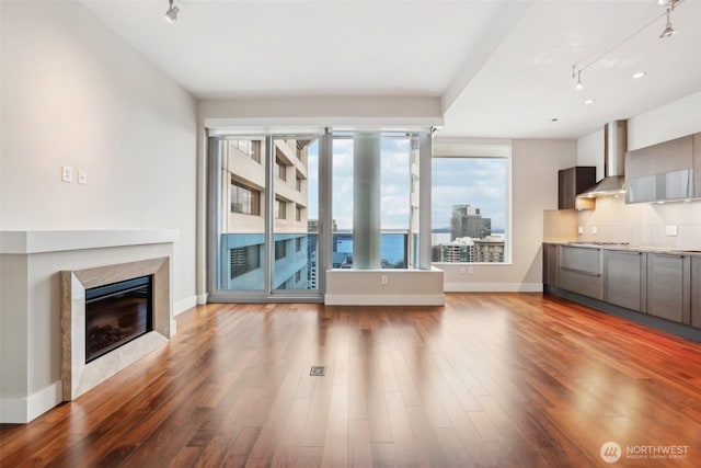 unfurnished living room with track lighting, baseboards, a premium fireplace, and wood finished floors